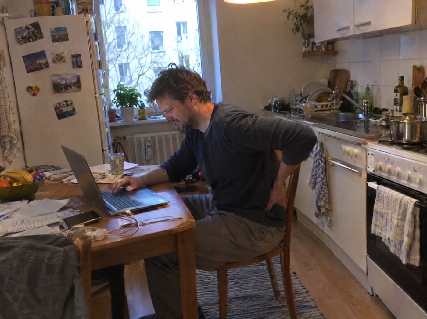 Mann mit Rückenschmerzen am Küchentisch im Homeoffice